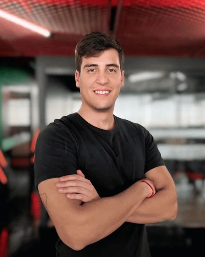 Ricardo Santos Mathia, o Kado, de braços cruzados e sorrindo, em pé num galpão.